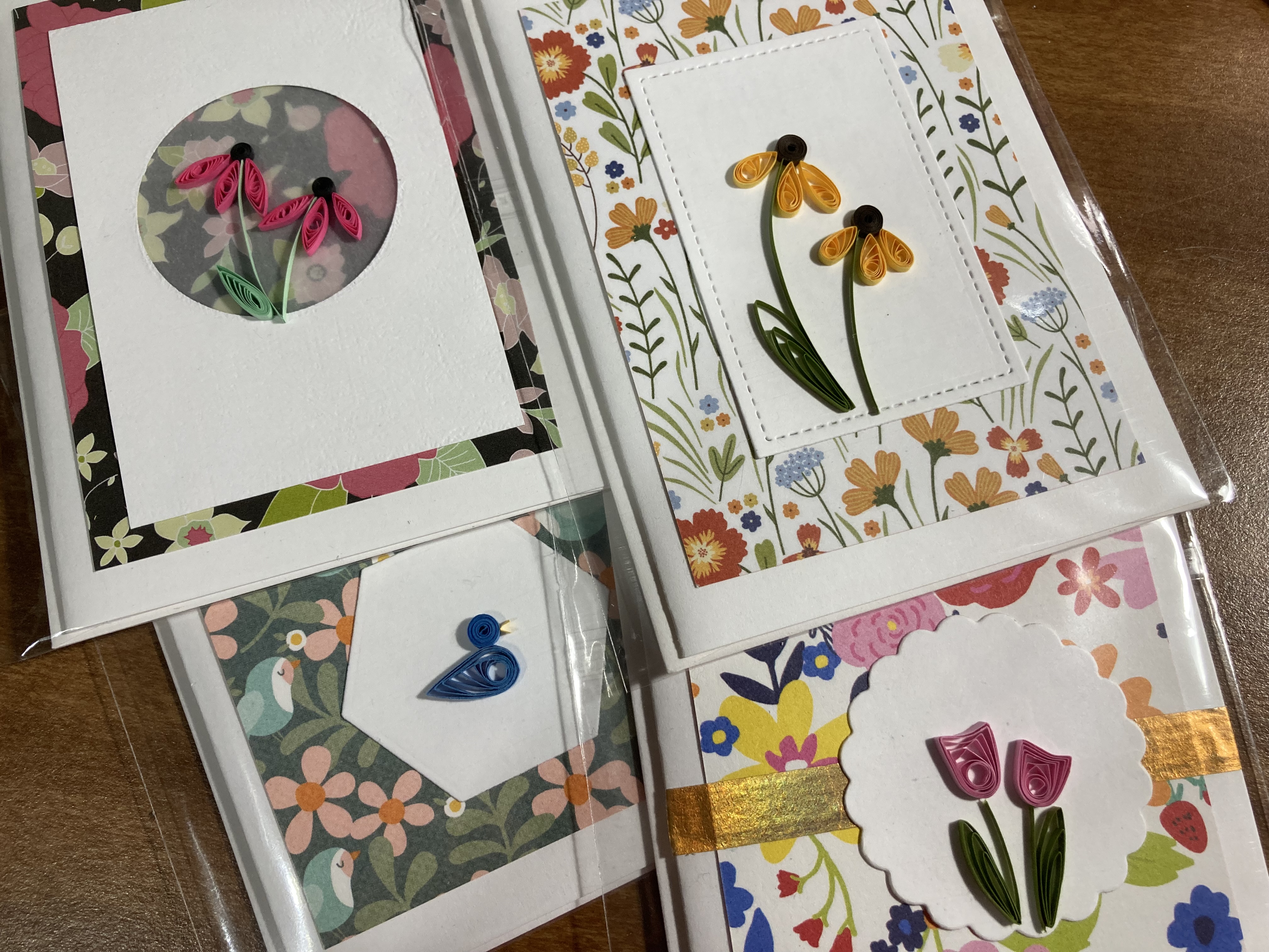  a picture of paper quilled greeting cards. One card features a pink flower with floral border, one has a yellow flower with floral border, one has a blue duck with floral border, and one has a pink tulip with floral border. 