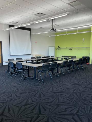 Meeting room B shown with rectangular table set-up, chairs around the table, and overhead projector and screen. 
