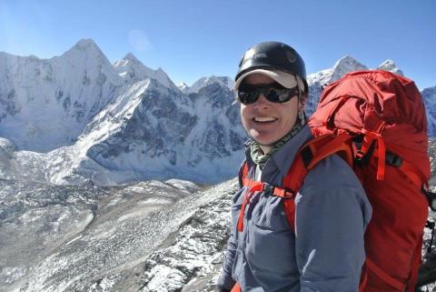 a photo of a woman with climbing gear on and a mountain in the background. 