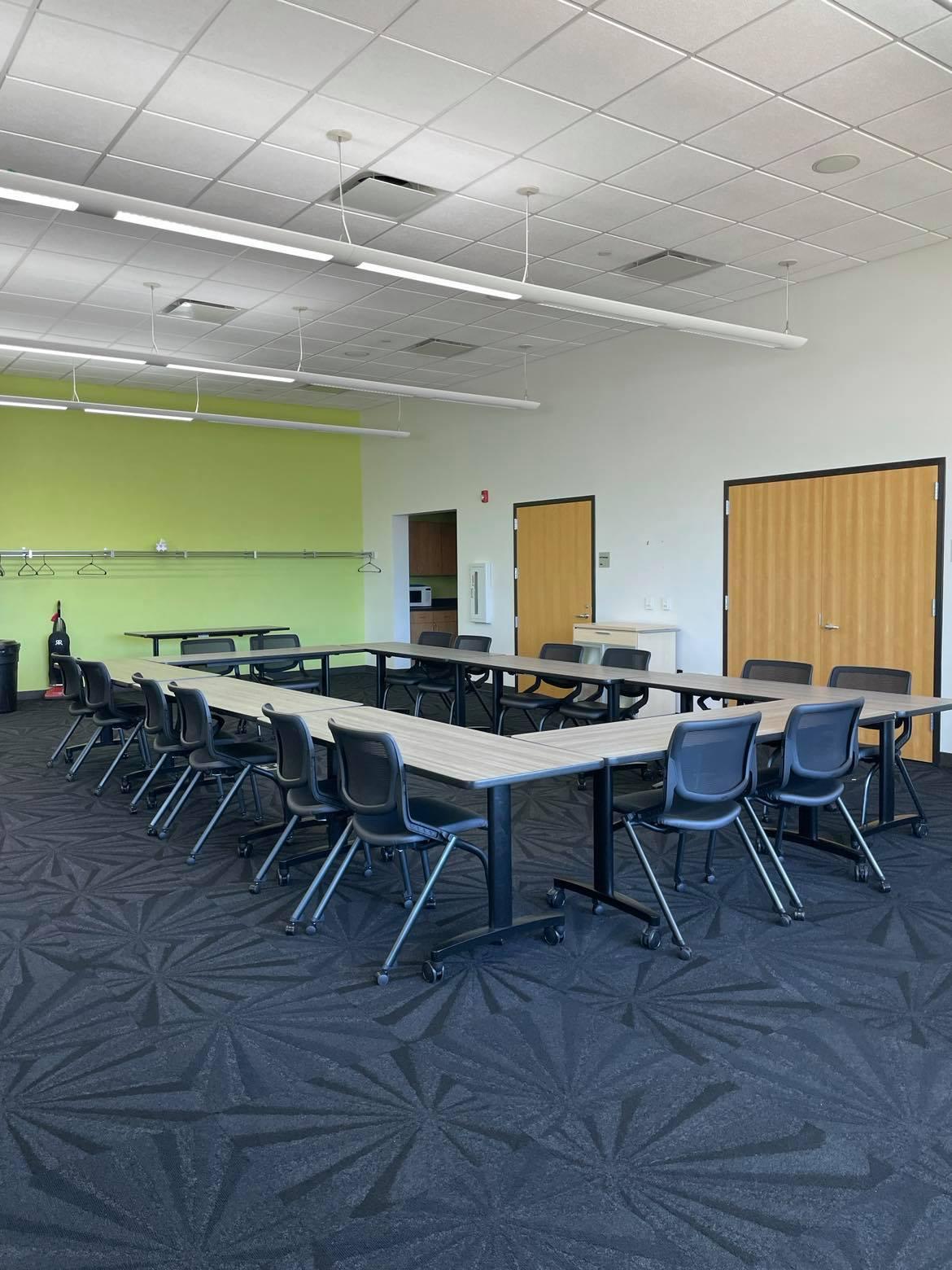 A photo of meeting room A with a rectangular table setup, chairs, and kitchenette. 