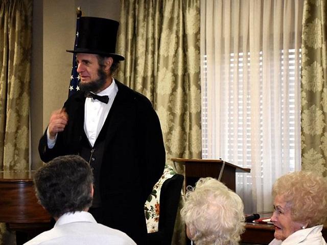 A photo of a man dressed up as Abraham Lincoln speaking in front of a crowd of people. 